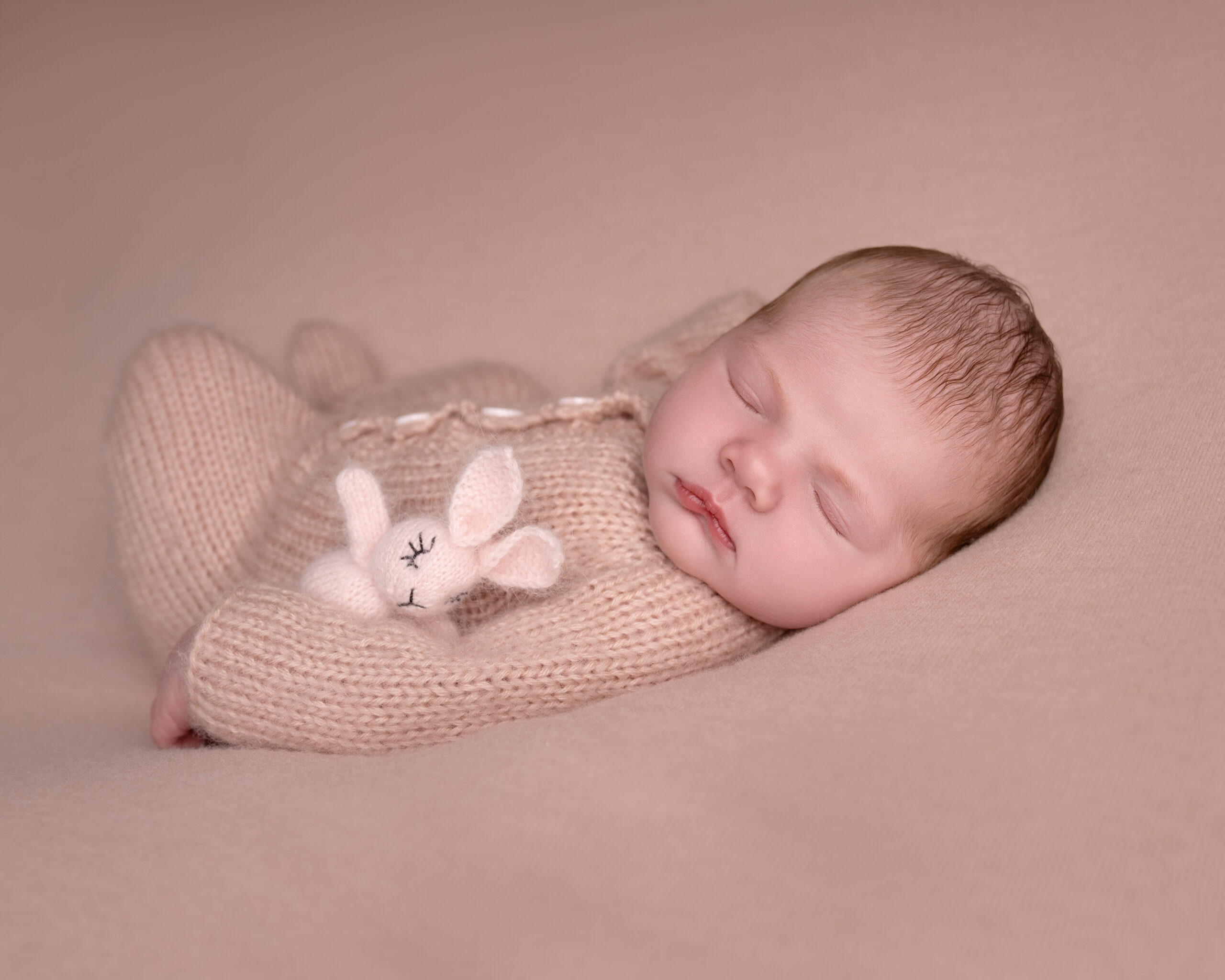 Nyfødt baby sover fredelig med bamse på rosa pledd.