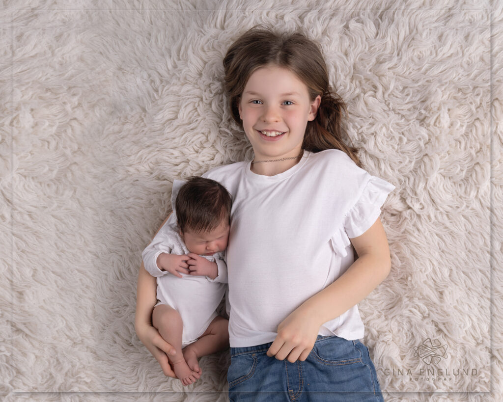 Storesøster holder nyfødt baby under familiefotografering i studio
