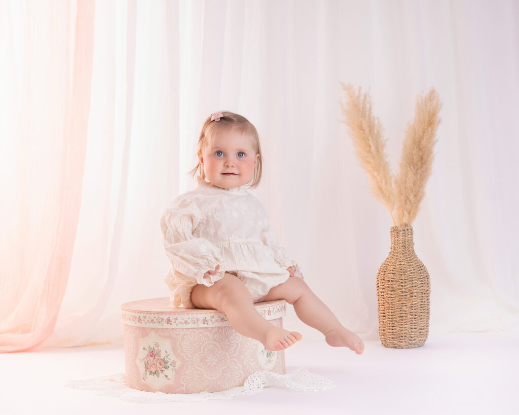 Babyjente sitter på vintageboks under babyfotografering i studio på Sofiemyr
